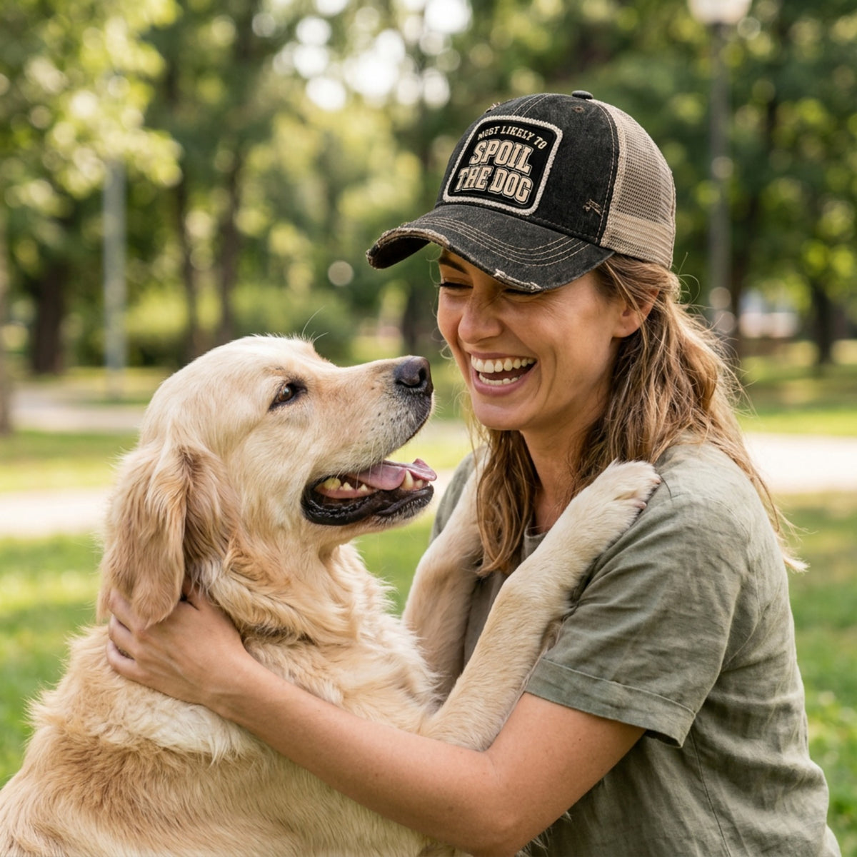 Woman hugging her golden retriever outdoors, wearing the black MOST LIKELY TO SPOIL THE DOG trucker hat